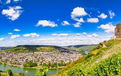 Burchtruïne Landshut op een wijngaardheuvel met uitzicht op Bernkastel-Kues en de Moezel onder een blauwe hemel met witte wolken.
