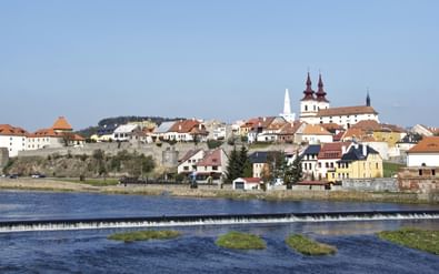 Panoramisch uitzicht op de stad Eger in Tsjechië met historische gebouwen en kerk met dubbele torens op een heuvel boven de Ohře met een stuw.