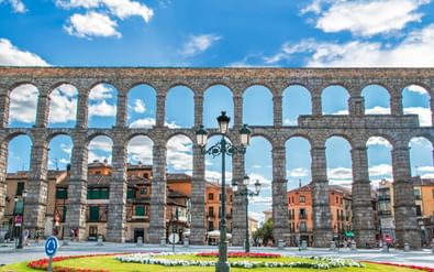 Romeins aquaduct van Segovia met bloementuin Het beroemde Romeinse aquaduct van Segovia met zijn dubbele stenen bogen boven een kleurrijke bloementuin en historische gebouwen.