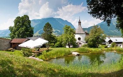 Schloss Kammer in Maishofen met vijver, witte kerk, stenen toren en bergachtergrond in Pinzgau, Oostenrijk.