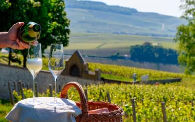 Champagne proeven in wijngaardlandschap Hand schenkt champagne in glazen op witte tafel met rieten mand, uitkijkend over Champagne wijngaarden en glooiende heuvels.