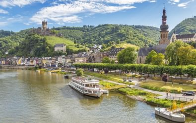 Schilderachtige Moezelvallei met rondvaartboot, historische stad, kerktoren en middeleeuws kasteel op wijngaardheuvels.