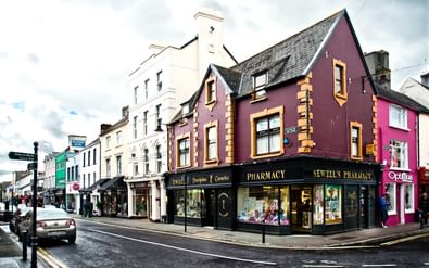 Killarney stadscentrum met kleurrijke gebouwen Straathoek in Killarney, Ierland met kleurrijke Victoriaanse gebouwen waaronder paarse Sewell's Pharmacy en roze winkelpuien met geparkeerde auto's.