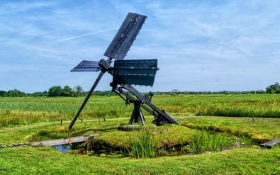 Historische houten windmolen met vier wieken in Nationaal Park Weerribben, omgeven door groene weilanden en wetlands onder blauwe lucht.