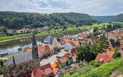 Luchtfoto van Stadt Wehlen met kerk, marktplein en huizen met rode daken langs de Elbe, omringd door groene heuvels.