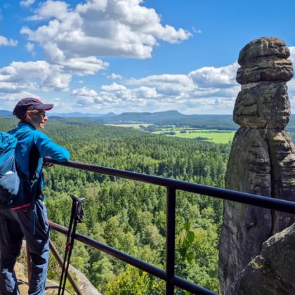 Wandelaar met rugzak bewondert panoramalandschap vanaf Pfaffenstein met opvallende rotsformatie en bebost dal eronder.