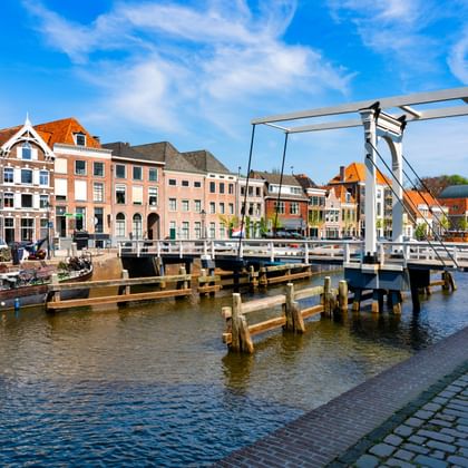Witte ophaalbrug over een gracht in Zwolle, Overijssel, met kleurrijke historische gebouwen en afgemeerde boten langs de waterkant onder een blauwe lucht.