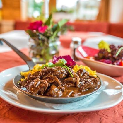 Traditionele goulash met mals vlees in rijke bruine saus geserveerd op wit bord met gele rijst en verse salade garnering.