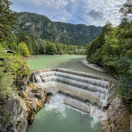 Lechfall stuw met getrapte betonstructuur die trapsgewijze watervallen creëert. Groene rivier stroomt door bebost dal met bergen.