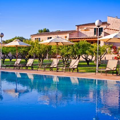 Finca Son Roig op Mallorca met groot blauw zwembad, ligstoelen met parasols en traditionele stenen gebouwen onder heldere hemel.