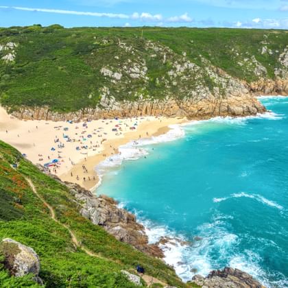 Luchtfoto van Porthcurno Beach in Cornwall met goudkleurig zand, turquoise zee en groene kliffen. Strandgangers op het zandstrand.