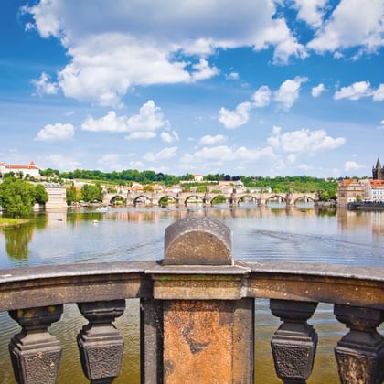 Uitzicht op de Karelsbrug over de Moldau in Praag met historische gebouwen en torens op de rechteroever, gezien vanaf stenen balustrade.