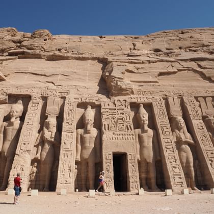 Oude Abu Simbel tempelfacade uitgehouwen in zandsteenrots met vier kolossale zittende beelden en hiërogliefen onder blauwe hemel.