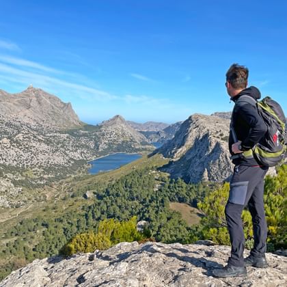 Wandelaar met rugzak staat op rotsuitstulping bij Ofre Pass nabij Soller, met uitzicht op Cúber reservoir en Tramuntana gebergte.