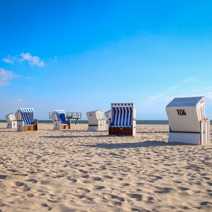 Traditionele Duitse strandkabines verspreid over zandstrand van Sylt. Blauw-wit gestreepte rieten manden genummerd 104 onder heldere hemel.