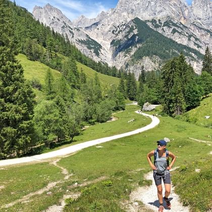 Vrouwelijke wandelaar op bergpad in Berchtesgadener Land met dramatische kalksteentoppen, groene alpenweiden en kronkelend pad door dal.