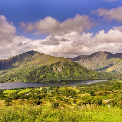 Glooiende groene heuvels en bergen rond een meer in Killarney National Park, Ierland, onder een dramatische bewolkte hemel.