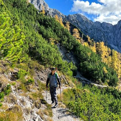 Christina wandelt op een bergpad bij Tarvisio met wandelstokken, omringd door herfstkleuren en dramatische kalkstenen pieken.