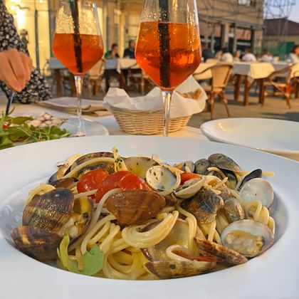 Bord spaghetti alle vongole met mosselen en kerstomaatjes geserveerd met oranje aperitief drankjes op een restaurantterras in Viareggio.