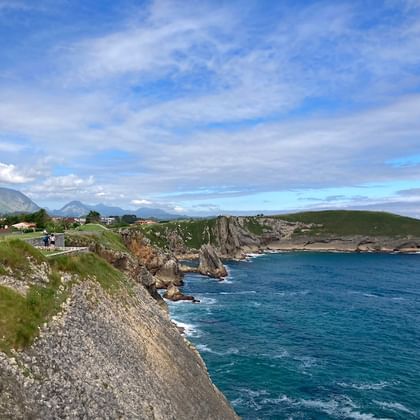 Dramatische kustlijn in Asturië, Noord-Spanje, met steile rotskliffen, turquoise zee en een kustdorp met bergen op de achtergrond.