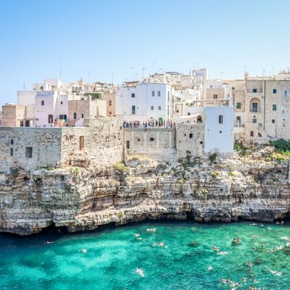 Polignano a Mare in Apulië: witte gebouwen op kalkstenen kliffen boven turquoise zee met zwemmers in een natuurlijke baai.
