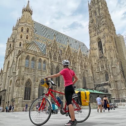 Fietser in rood shirt met toerfiets en gele fietstassen voor de Stephansdom in Wenen op een zonnige dag.