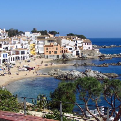 Schilderachtig uitzicht op Calella de Palafrugell met witte mediterrane huizen langs een zandstrand en rotsachtige kust met helder blauw water.