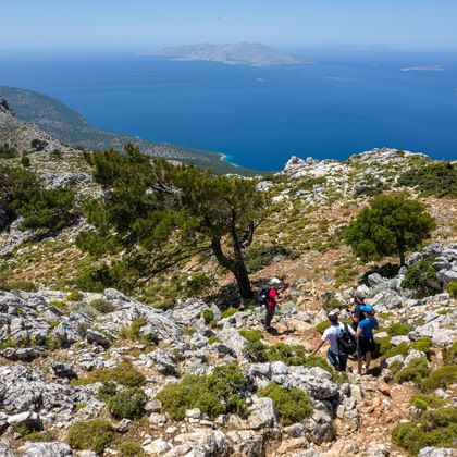 Wandelaars op rotsachtig bergpad op Rhodos, Griekenland, met blauwe Egeïsche Zee en verre eilanden op de achtergrond.
