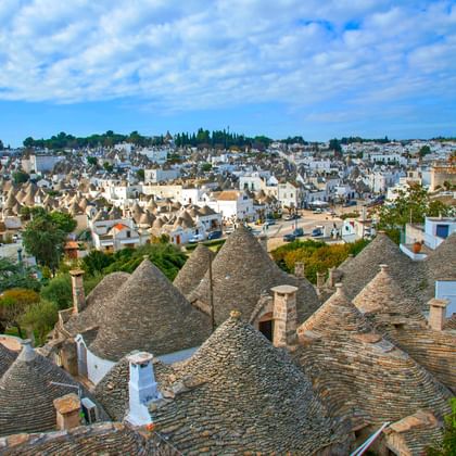 Panoramisch uitzicht op Apulië met traditionele trulli huizen met kegelvormige stenen daken op de voorgrond en witte gebouwen in de stad.