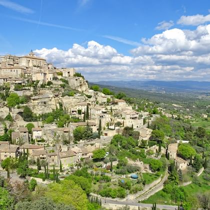 Panoramisch uitzicht op Gordes, een heuveltopdorp in de Provence met stenen gebouwen die de helling afdalen, omringd door groene valleien.