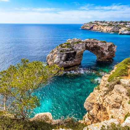 Es Pontàs natuurlijke steenboog rijst op uit turquoise water op Mallorca, omgeven door rotsachtige kliffen met groene vegetatie.