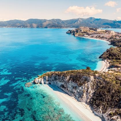 Luchtfoto van de Elba kust met turquoise Middellandse Zee wateren, witte zandstranden, rotsachtige kliffen en bergachtig landschap.