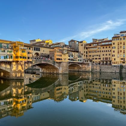 Ponte Vecchio brug met middeleeuwse gebouwen over de Arno in Florence. Perfecte spiegeling in kalm water onder blauwe lucht.