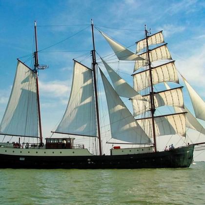 Driemast zeilschip Simmer Fan Fryslân met witte zeilen op kalm water onder blauwe hemel met wolken.