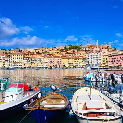 Kleurrijke haven van Portoferraio op Elba met vissersboten op voorgrond en pastelkleurige gebouwen op heuvel.