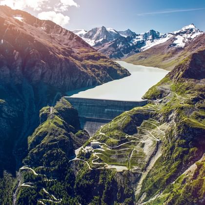 Luchtfoto van de Grande-Dixence dam in een vallei omringd door besneeuwde Alpentoppen en groene berghellingen.