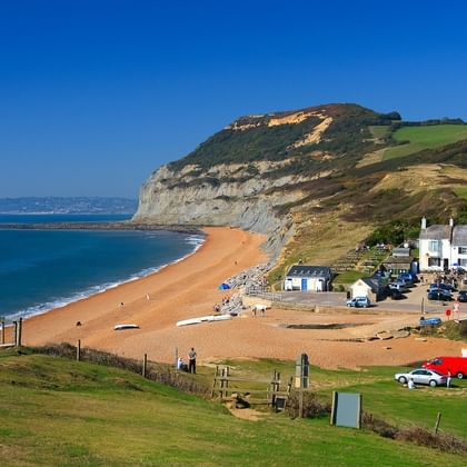 Seatown strand aan Dorsets Jurassic Coast met goudkleurig zand, dramatische gelaagde kliffen, witte kusthuizen en kalme blauwe zee.