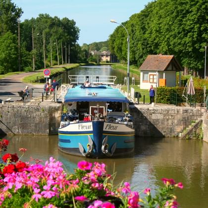 MS Fleur boot in een sluis in Frankrijk met kleurrijke bloemen op de voorgrond, stenen sluismuren en een met bomen omzoomde waterweg.