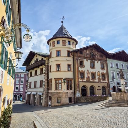Historisch marktplein in Berchtesgaden met kleurrijke Alpengebouwen, ronde toren met kegeldak, beschilderde gevels en kasseien.
