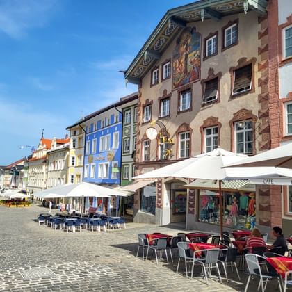 Geplaveide voetgangerszone in Bad Tölz met kleurrijke historische gebouwen, café-terrassen en witte parasols onder blauwe lucht.