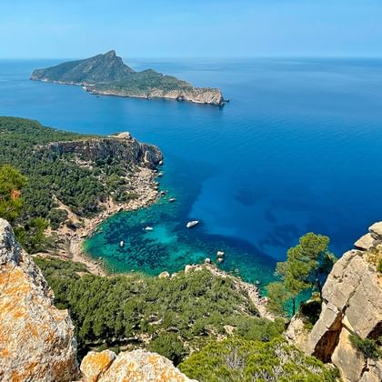 Panoramisch uitzicht vanaf rotsachtige kliffen bij Sant Elm, Mallorca, met turquoise Middellandse Zee, beboste kust en een bergachtig eiland.