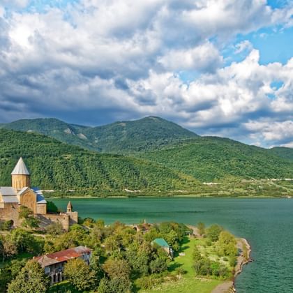 Ananuri vesting met stenen torens en kerk met uitzicht op een groot bergmeer, omgeven door groene beboste heuvels onder bewolkte hemel.