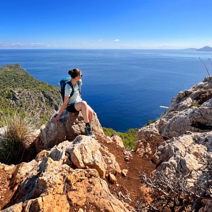 Vrouwelijke wandelaar met rugzak zittend op rotsachtige klif met uitzicht op blauwe Middellandse Zee op Trans Tramuntana op Mallorca.