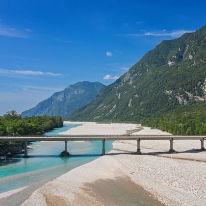 Brug over de turquoise Tagliamento bij Venzone met witte grindbanken en groene bergen op de achtergrond onder blauwe lucht.