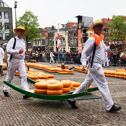 Alkmaarse kaasmarkt met traditionele dragers Twee mannen in witte uniformen en gele hoeden dragen kaaswielen op groene houten dragers op Alkmaars traditionele kaasmarkt.