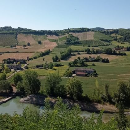 Panoramisch uitzicht op glooiende heuvels in Emilia-Romagna met lappendeken van velden, wijngaarden, verspreide boerderijen en een vijver.