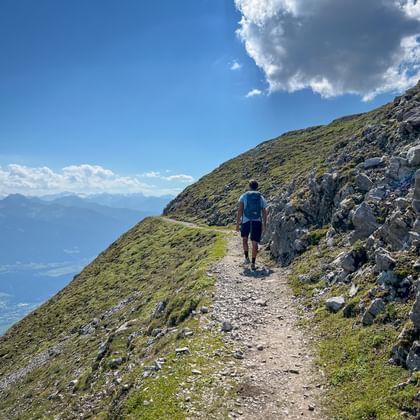 Wandelaar in blauw shirt op bergpad bij Karwendel met panoramisch uitzicht op vallei en rotsachtige kalksteenkliffen onder bewolkte hemel.