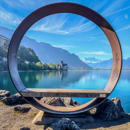 Cirkelvormige metalen sculptuur omlijst zicht op Kasteel Chillon aan het Meer van Genève. Bergen en blauwe lucht op achtergrond. Montreux promenade.