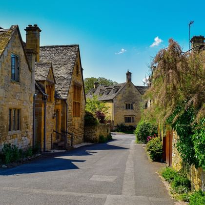 Traditionele Cotswolds stenen huizen met leien daken langs een rustige dorpsstraat in Bourton-on-the-Water, omgeven door weelderige vegetatie.