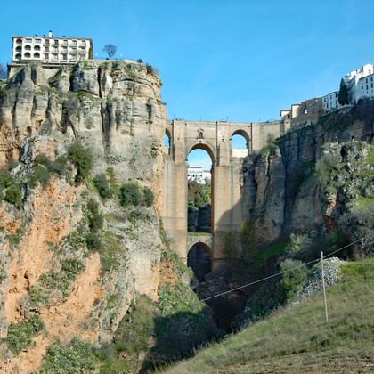 De historische Puente Nuevo brug in Ronda overspant een diepe rotskloof en verbindt witte gebouwen op beide kliffen onder een blauwe hemel.
